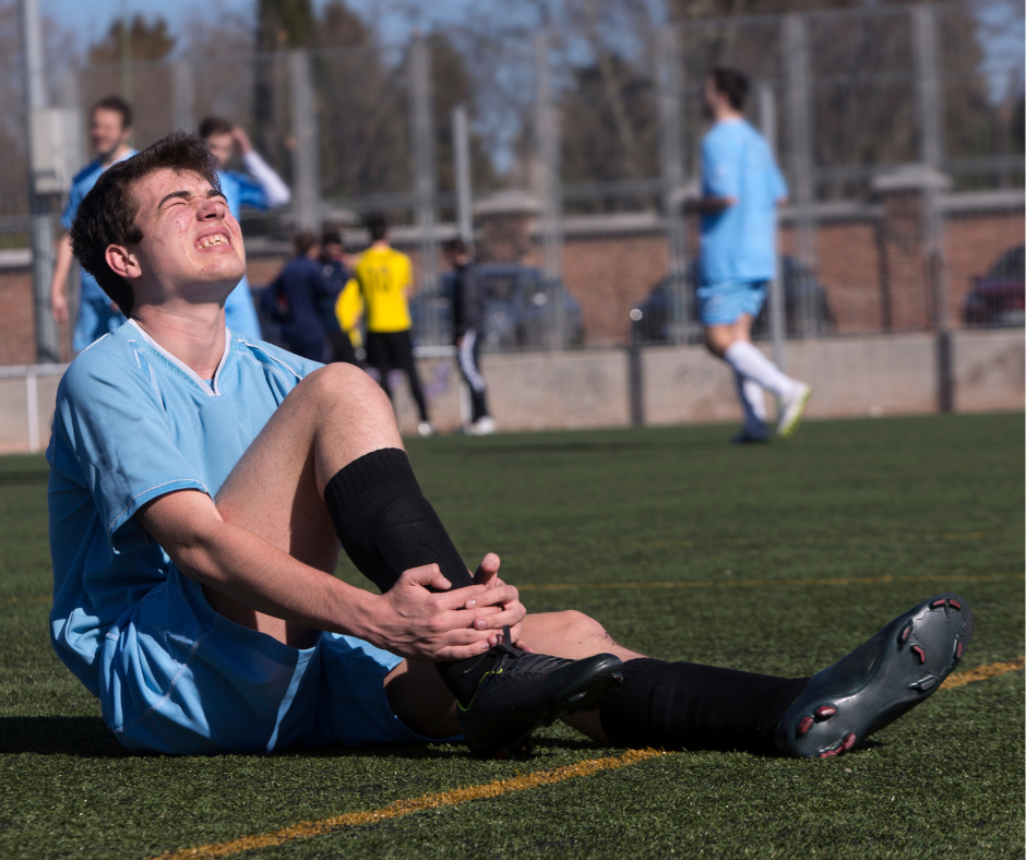 Boy playing soccer with painful expression on face holding onto his ankle that has an injury